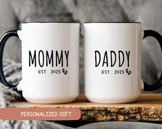 two coffee mugs with the words mommy and daddy printed on them sitting on a wooden table