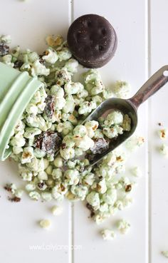 a green cup filled with popcorn next to a spoon and chocolate covered cookie on the table