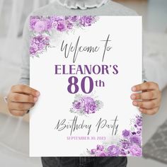 a person holding up a sign that says welcome to eleanor's 80th birthday party