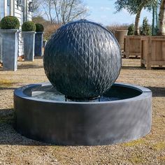 a large metal ball sitting on top of a water fountain in a yard next to potted trees