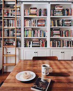 a wooden table topped with a cup of coffee next to a book shelf filled with books