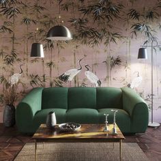 a green couch sitting in front of a wall with birds on it