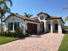 a white house with brick driveway and palm trees