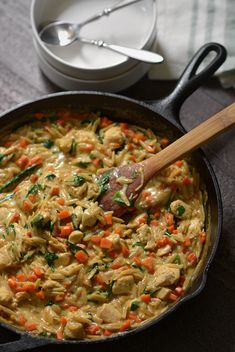 a skillet filled with chicken and carrots on top of a table