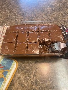 a chocolate cake in a glass dish with a spatula on the counter next to it