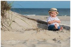 a baby sitting in the sand at the beach with his hat on and mouth wide open