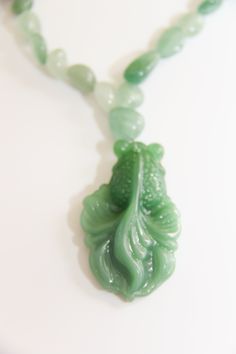 Hand carved big green glass Koi fish pendant dangling from small green Aventurine/jade nuggets necklace. 16" Whimsical Hand-Carved Glass Green Koi Fish Pendant: The Asian Koi fish is very spiritual and very lucky in all aspects of your life. Koi fish is the Chinese symbol of good luck, prosperity, & Tranquility. According to Feng Shui, a fish represents wealth and prosperity because the actual word in Chinese for fish, in Pinyin: yú, 魚, also translates to “abundance” The color green associated with the heart chakra is Green. Green symbolizes harmony, creativity, health, abundance and nature. Green Aventurine: Aventurine meaning comes from the Italian word Aventura which means chance, a hint at the great fortune this stone can bestow upon you. Aventurine is a stone of prosperity. It reinfor Unique Green Carved Necklace, Spiritual Single Strand Jade Necklace, Spiritual Jade Necklace For Good Luck, Green Carved Amulet Necklace, Handmade Jade Necklaces For Good Luck, Unique Green Necklace With 108 Beads, Adjustable Green Carved Necklace, Adjustable Green Carved Necklaces, Green Jade Amulet Necklace