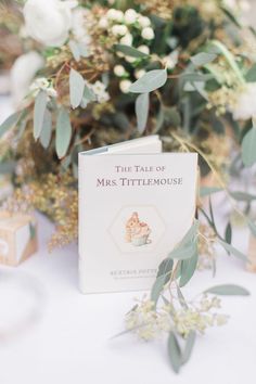 the tale of mrs tittlemous book on a table with flowers and greenery