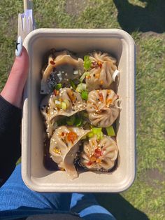 a person holding up a white container filled with dumplings and vegtables