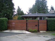 a wooden fence in front of a house with trees and bushes on the other side