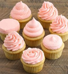 six cupcakes with pink frosting sitting on a wooden table