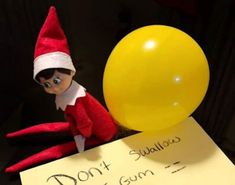 an elf is sitting next to a yellow balloon and a sign that says, don't gum on it