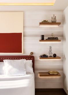 a bed with white sheets and pillows in a room that has shelves on the wall