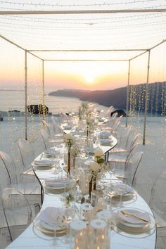 a long table is set with white plates and silverware for an outdoor wedding reception