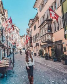 a woman is standing in the middle of an alleyway with flags flying above her