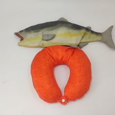 a stuffed fish sitting on top of an orange pillow next to it's head