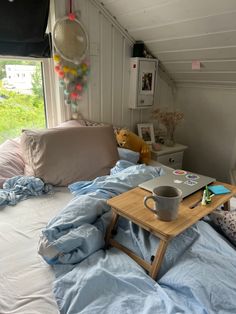 a bed with blue sheets and pillows in a room next to an open window that has a laptop on it