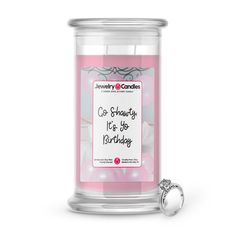 a pink birthday candle with a ring on the lid and congratulations card in front of it