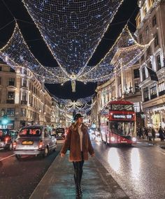 a woman is walking down the street in front of christmas lights and double decker buses