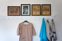 three framed pictures hang on the wall above a coat rack with two towels hanging from it