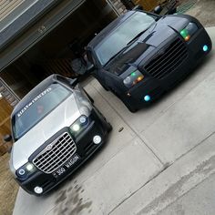 two cars parked next to each other in front of a garage with their lights on