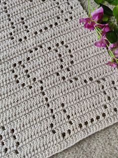 a crocheted blanket with purple flowers on the floor next to it and a pink flower