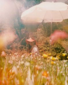 a woman sitting in the grass with an umbrella over her head and flowers around her