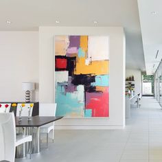 an abstract painting hangs on the wall next to a dining room table with white chairs