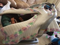 a baby in a car seat covered with a blanket and some toys on the floor