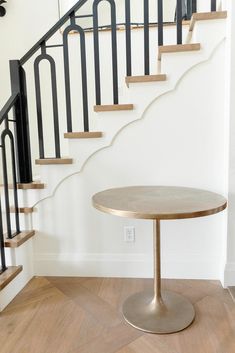 a round wooden table sitting in front of a stair case next to a banister