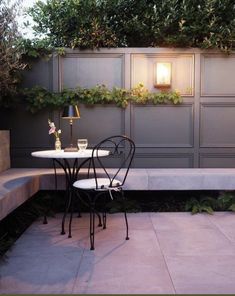 a table and chair sitting on top of a patio next to a wall covered in plants