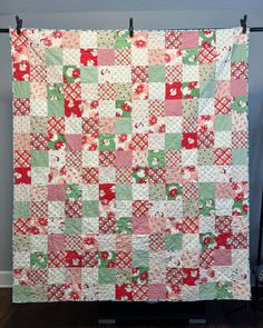 a quilt hanging on a clothes line in front of a blue wall with a red and green checkerboard pattern