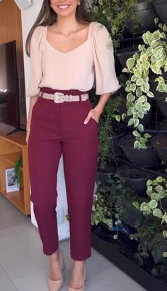 a woman standing in front of a green wall wearing red pants and a pink top