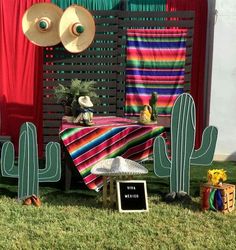 an outdoor area with cactus decorations, hats and blankets on the grass in front of a red curtain