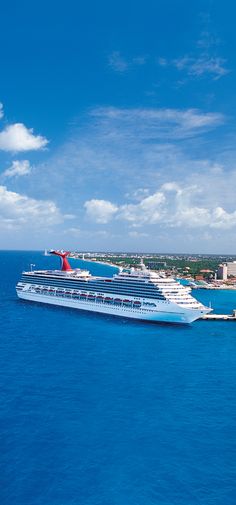 a large cruise ship in the middle of the ocean with buildings on either side and blue skies above