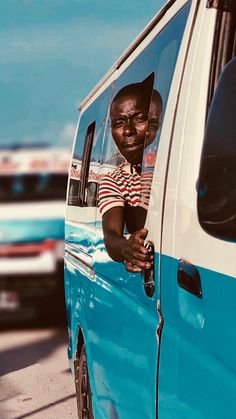 a man sitting in the driver's seat of a blue and white van with other cars behind him