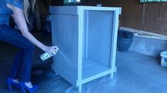 a woman in blue high heels spray painting a cabinet