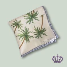 "Discover the allure of tropical elegance with Gilberti Silk Arts' captivating palm tree design silk pocket square, enhanced by a stylish light blue border. This refined accessory seamlessly blends the charm of exotic vibes with a touch of sophistication, making it a versatile addition to your wardrobe. Crafted from high-quality 100% silk twill with hand-rolled hems, this pocket square not only offers a luxurious feel but also exudes polished style. Whether you're attending a beach wedding, a su Luxury Elegant Silk Handkerchiefs, Jamaican Wedding, Palm Tree Design, Silk Handkerchief, Polished Style, Art Scarves, Blue Border, Silk Pocket Square, Silk Art