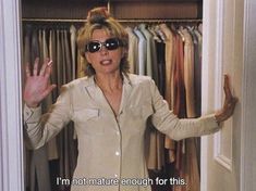 a woman wearing sunglasses standing in front of a closet full of clothes with her hands up