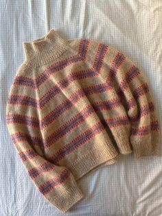 an old sweater laying on top of a bed with white sheets and blue and red stripes