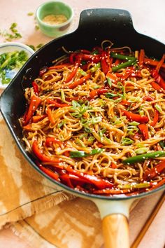 a wok filled with noodles and vegetables on top of a wooden cutting board next to some chopsticks