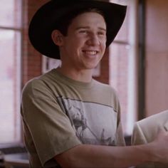 a young man wearing a black cowboy hat and holding a piece of paper in his hand