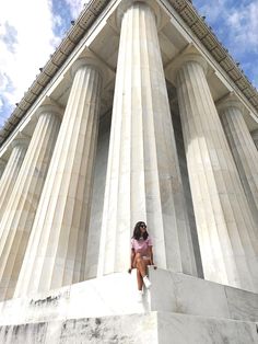 a woman sitting on top of a white pillar next to a tall building with columns