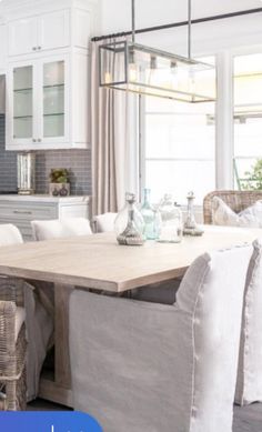 a dining room table and chairs in front of an open kitchen area with white cabinets