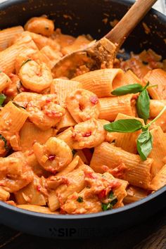 a skillet filled with pasta and spinach on top of a wooden table next to a spoon