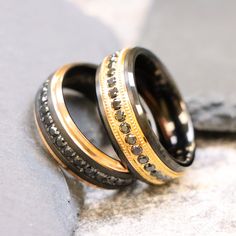 two gold and black wedding rings sitting on top of a stone slab with diamonds in them