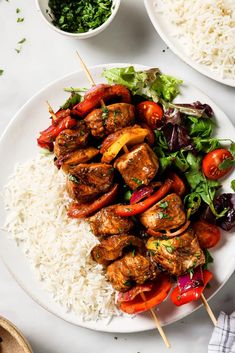 a white plate topped with meat and veggies on skewers next to rice