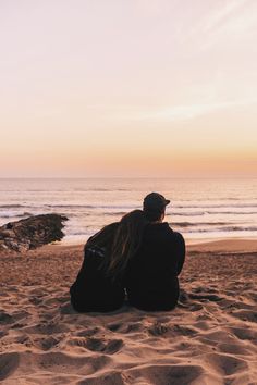 two people sitting on the beach watching the sunset