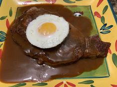 a plate topped with meat covered in gravy and an egg on top of it