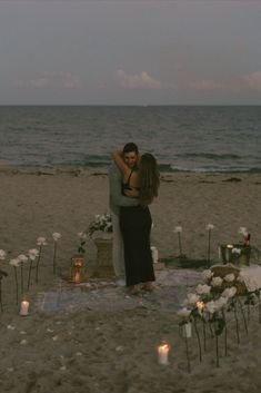 a couple embracing each other on the beach with candles in front of them and flowers all around